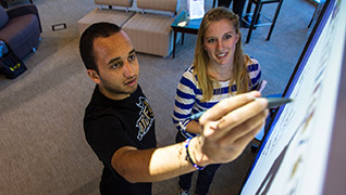 Male and female student drawing on whiteboard 