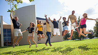 8 students in mid jump outside with hands in the air